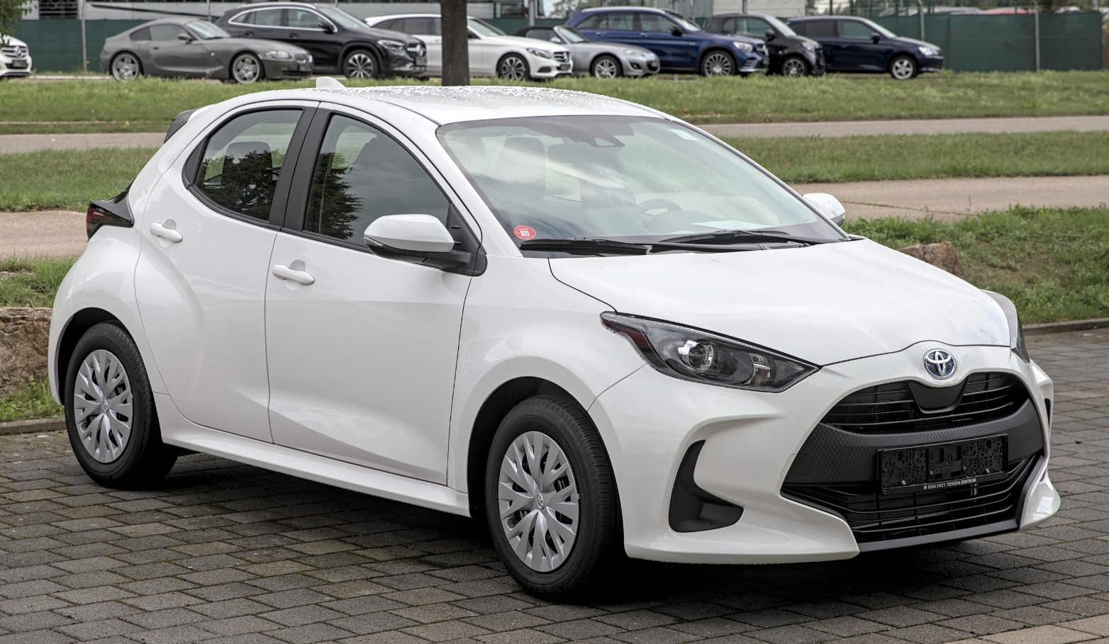 Toyota Yaris Hybrid, vedere lateral-frontală, hatchback alb, parcat în exterior