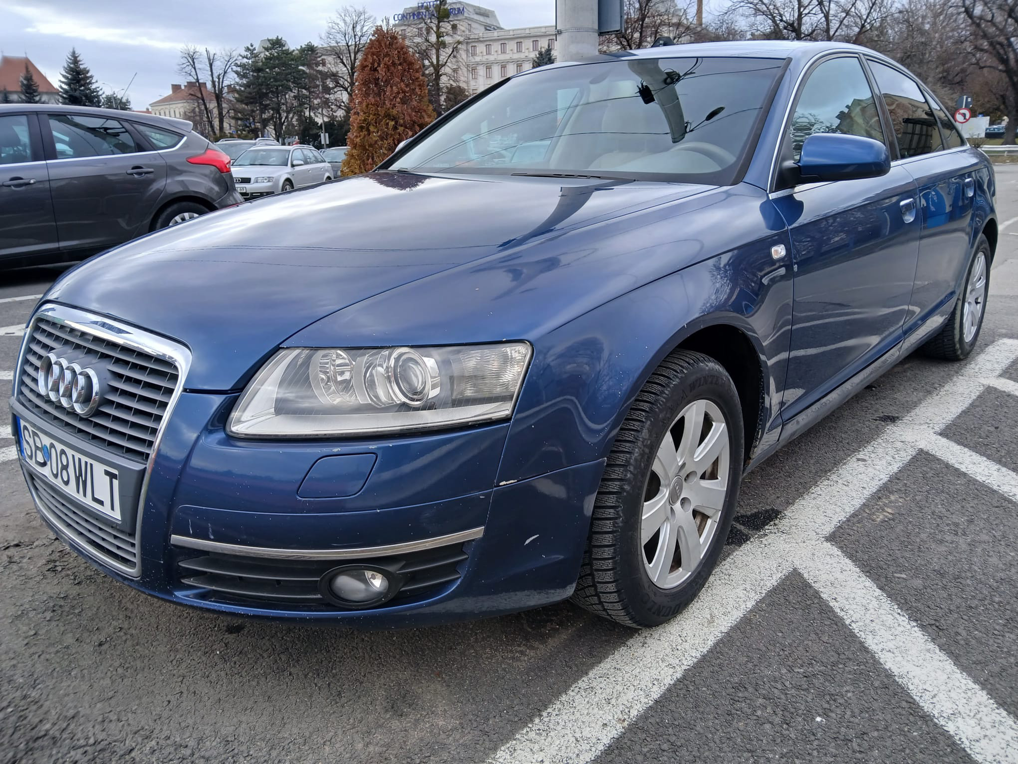 Audi A6 albastru parcat, vedere față laterală, într-o zonă urbană